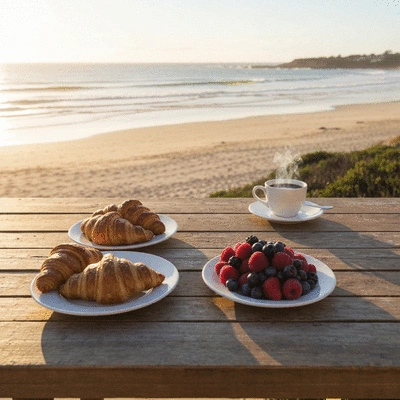 A delicious breakfast spread on a table overlooking Cottesloe Beach at sunrise, with coffee, pastries, and fresh fruit.